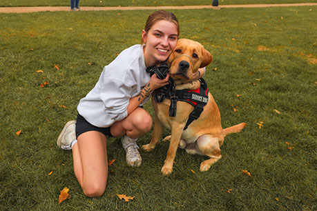 A student hugging a service dog. Links to What to Give