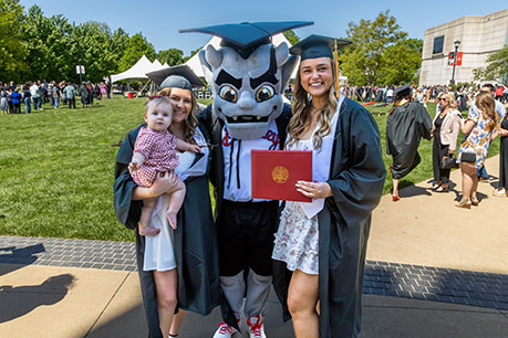 Graduates posing with the mascot. Links to Gifts That Pay You Income 